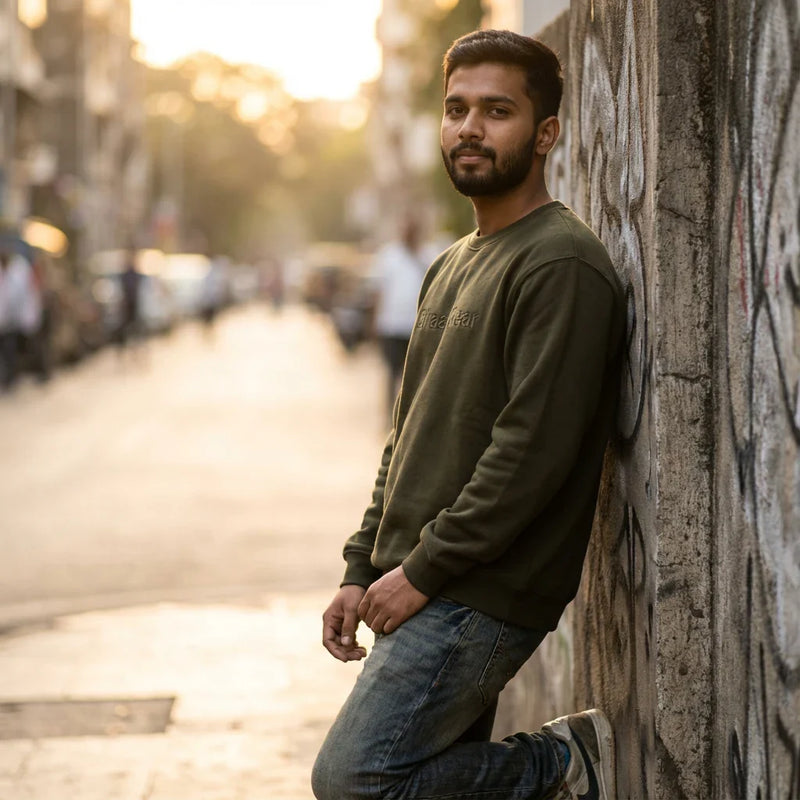 Indian male model wearing a BhaariGear sweatshirt against a concrete street wall, casual street-style fashion.