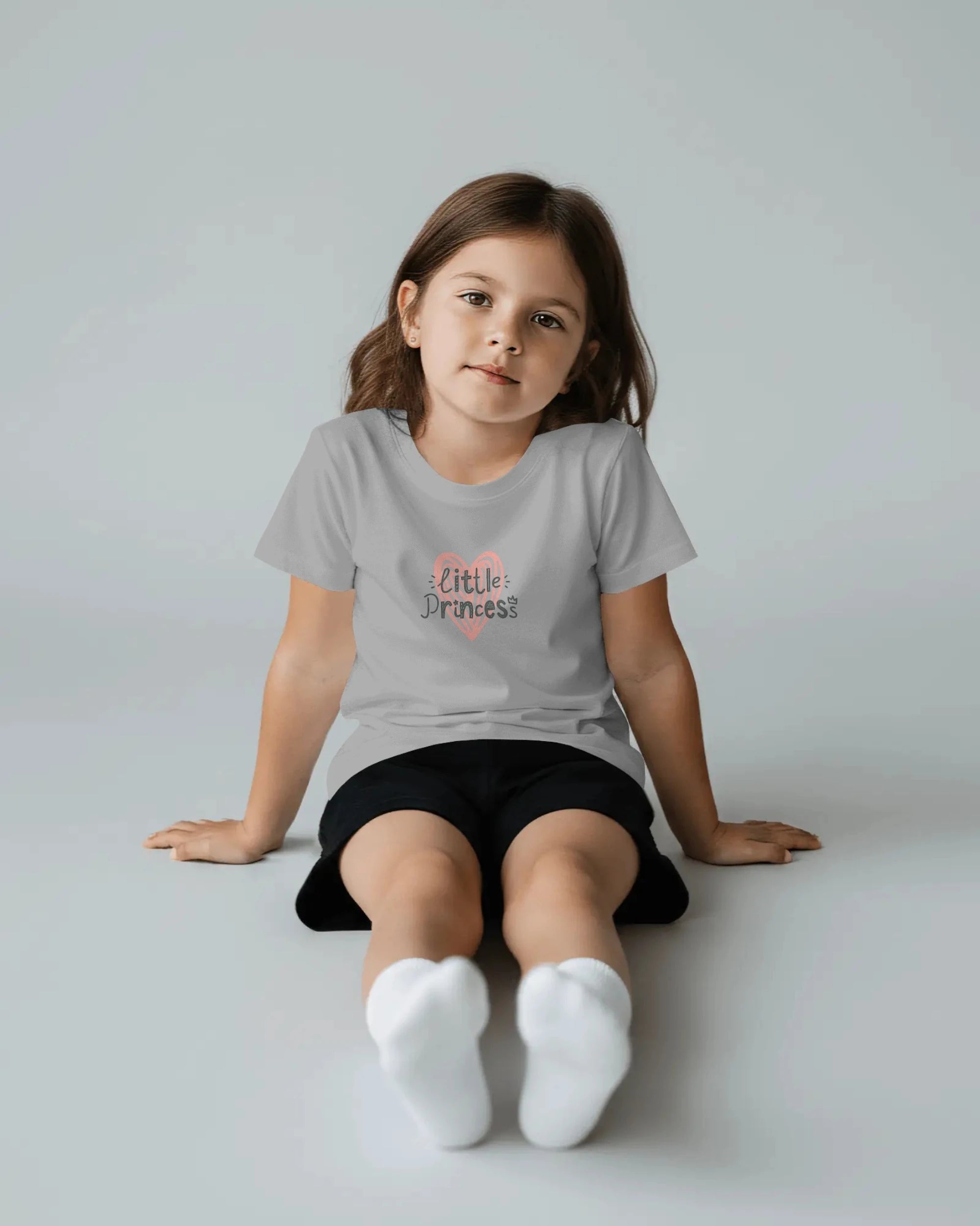 Young girl wearing a gray t-shirt with 'Little Princess' text, sitting on a light gray background.