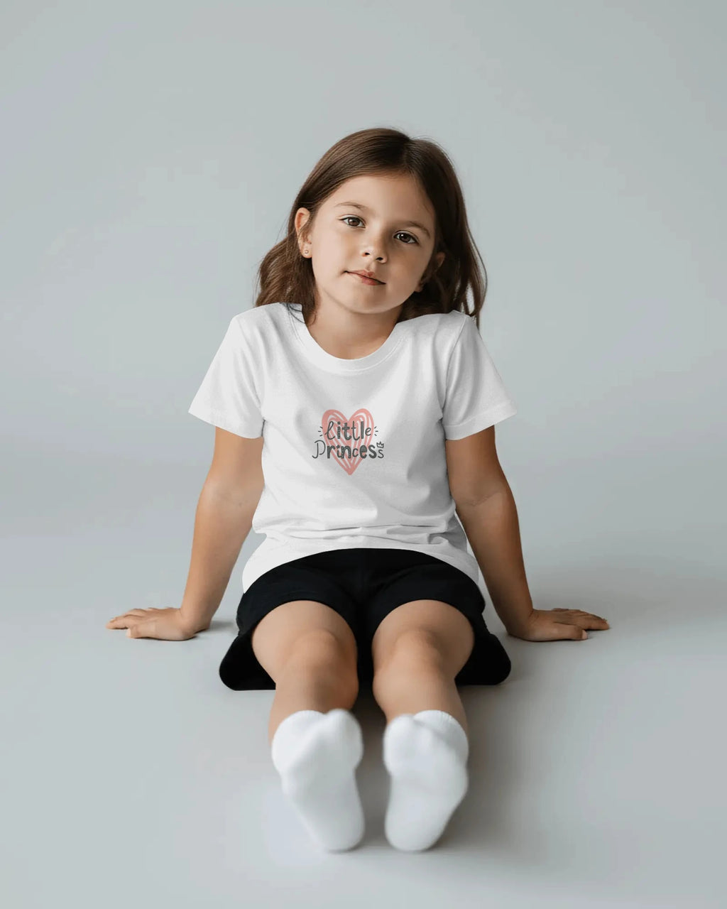 Young girl wearing a white t-shirt with 'Little Princess' text on a plain background