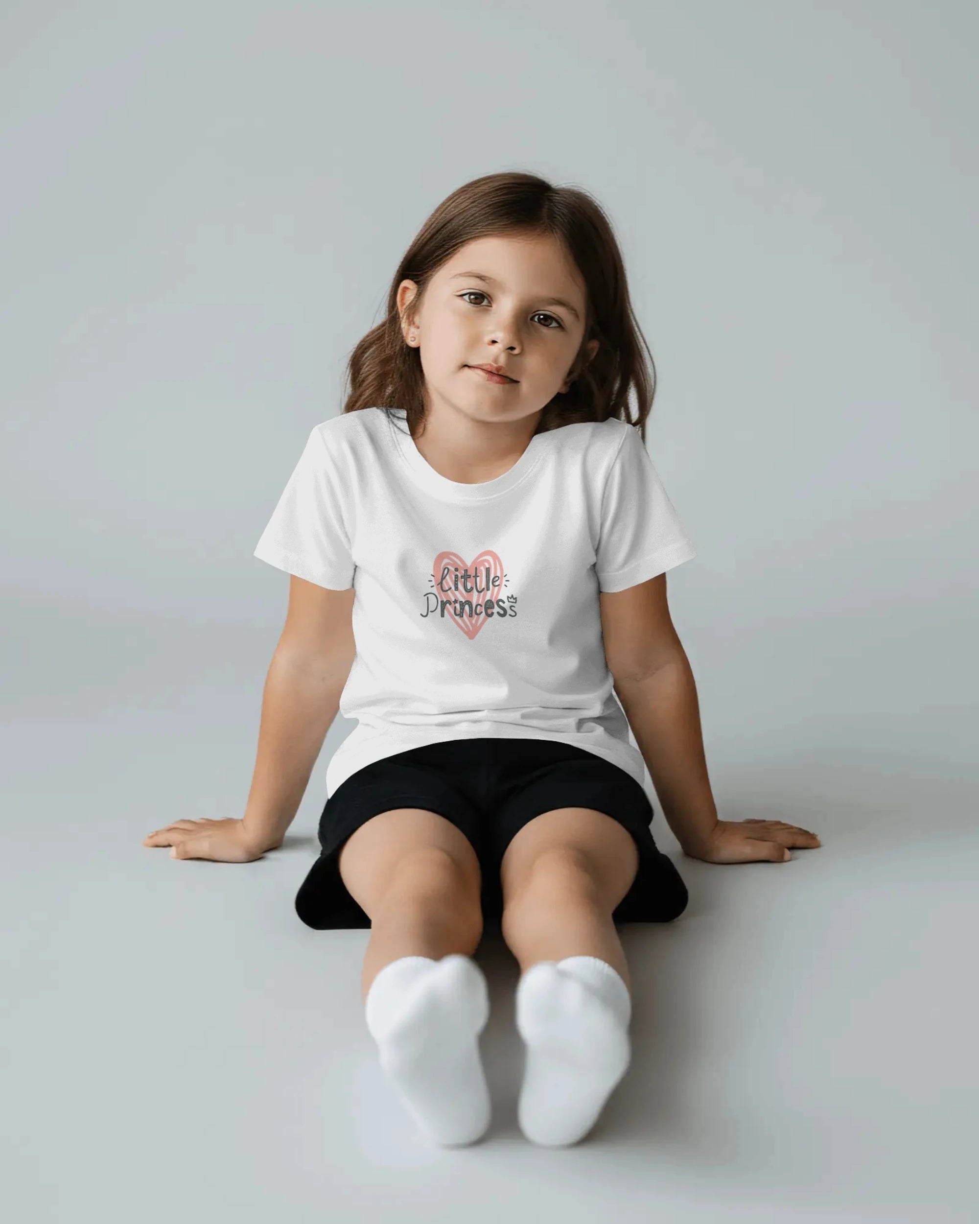 Young girl wearing a white t-shirt with 'Little Princess' text on a plain background