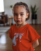 Child wearing an orange t-shirt with a graphic design and text indoors.