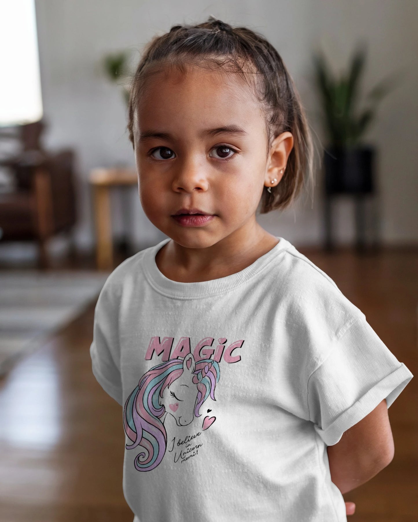 Child wearing a white t-shirt with a unicorn graphic and 'Magic' text in a home setting.