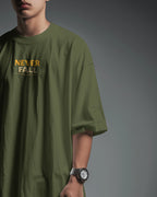 Olive green oversized T-shirt with "Never Fall Warrior Legacy" graphic by BhaariGear, front view, casual fit, soft fabric.