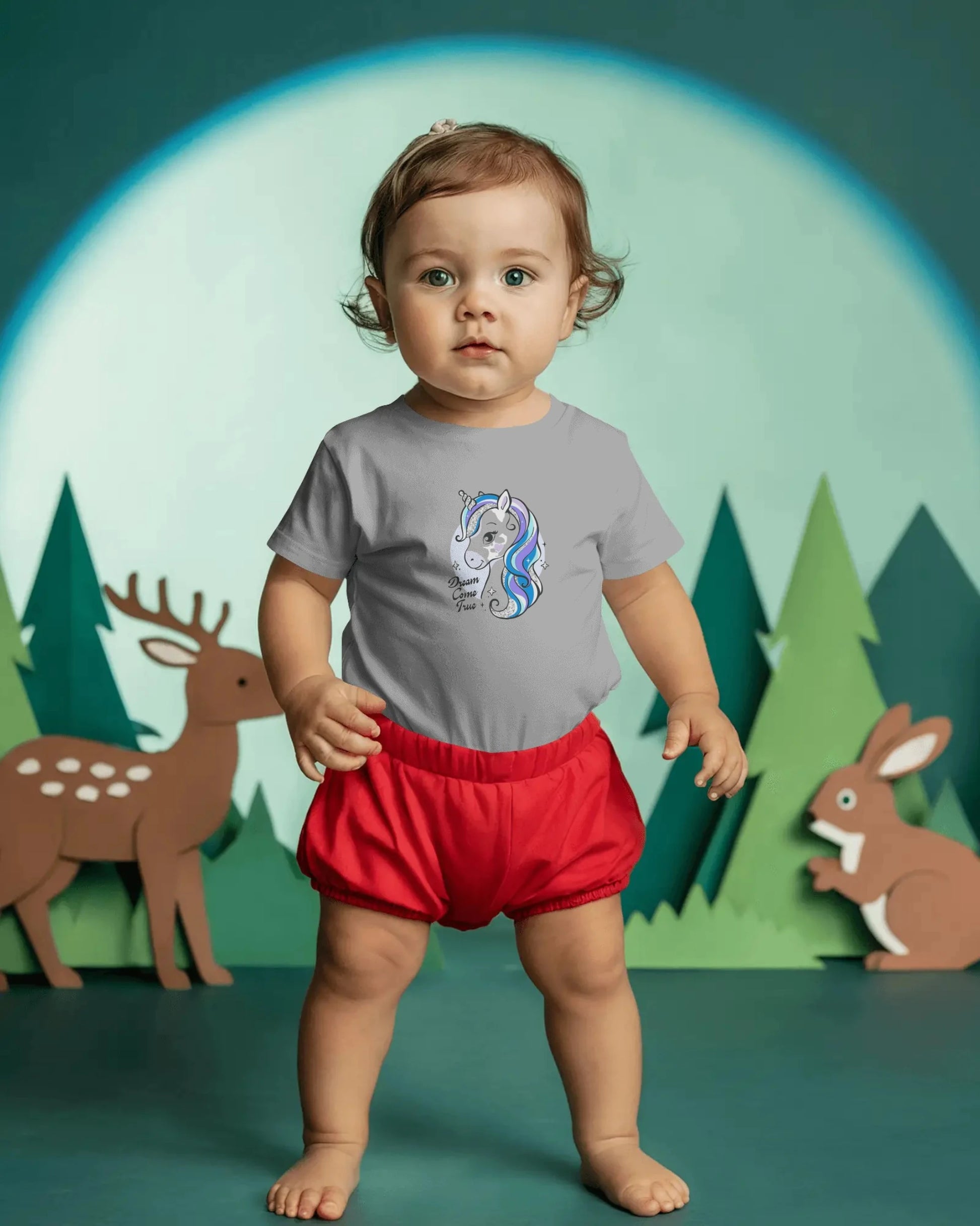 Child wearing a gray shirt with a colorful design and red shorts in front of a forest background