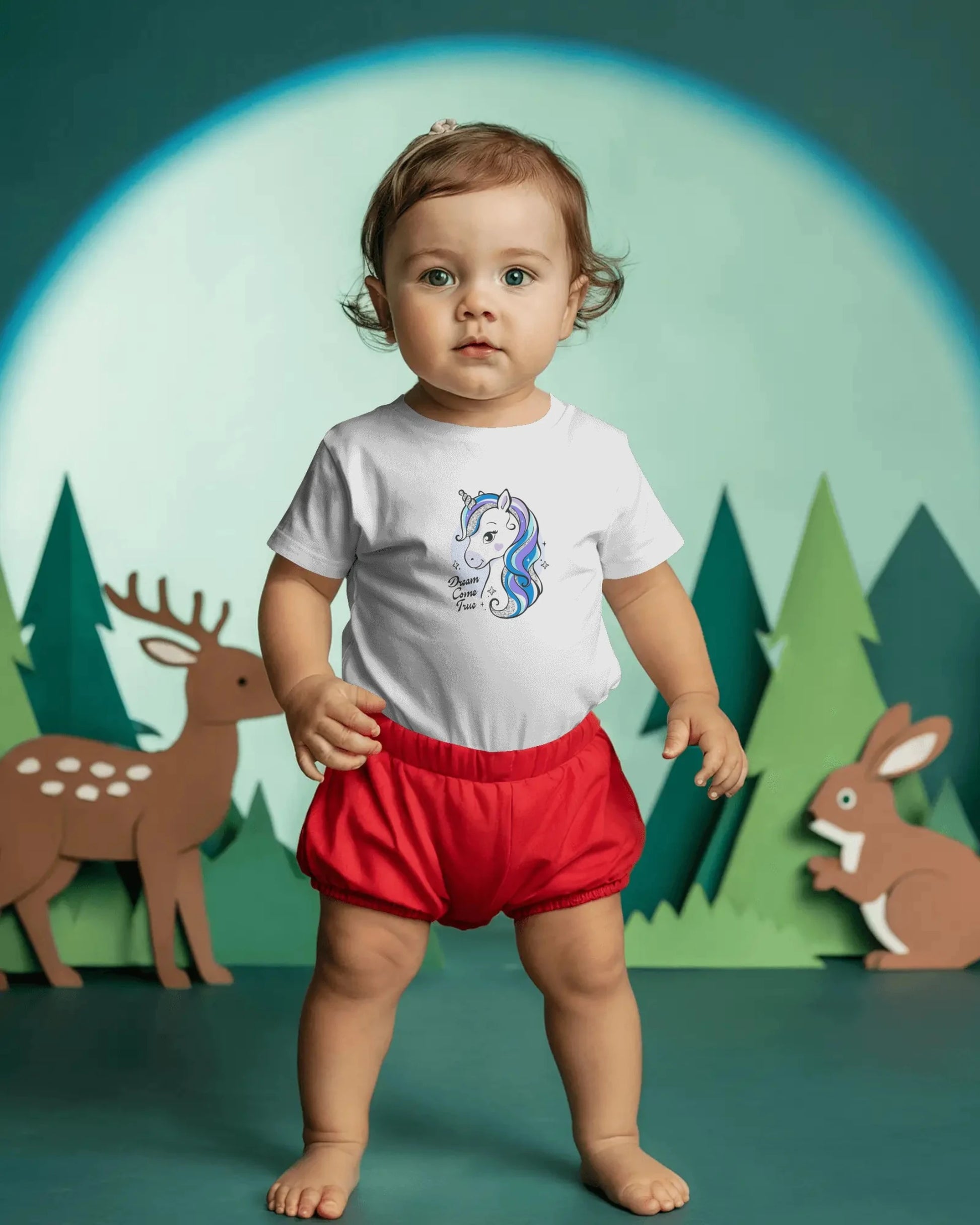 Child wearing a white shirt with a blue design and red shorts in front of a forest background