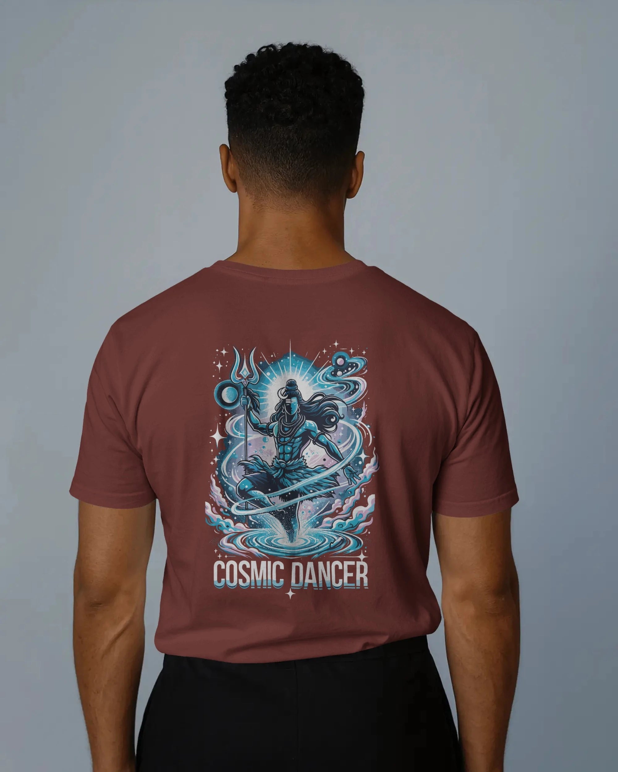 Person wearing a brick red t-shirt with 'Cosmic Dancer' design on the back against a gray background