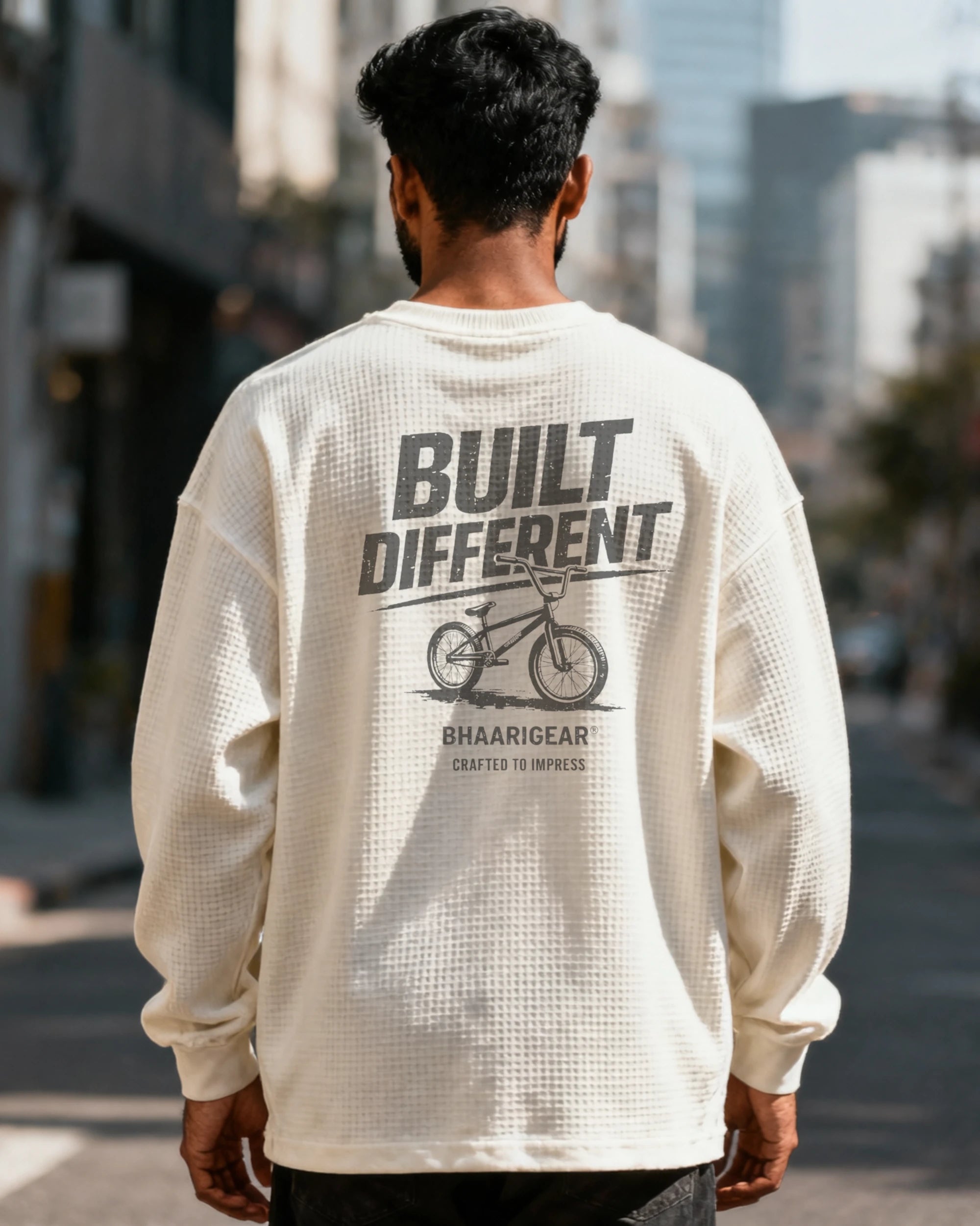 Person wearing a cream long-sleeve shirt with 'Built Different' text and graphic, standing on a city street.