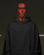Person wearing a black pull over hoodie with red face paint against a dark background