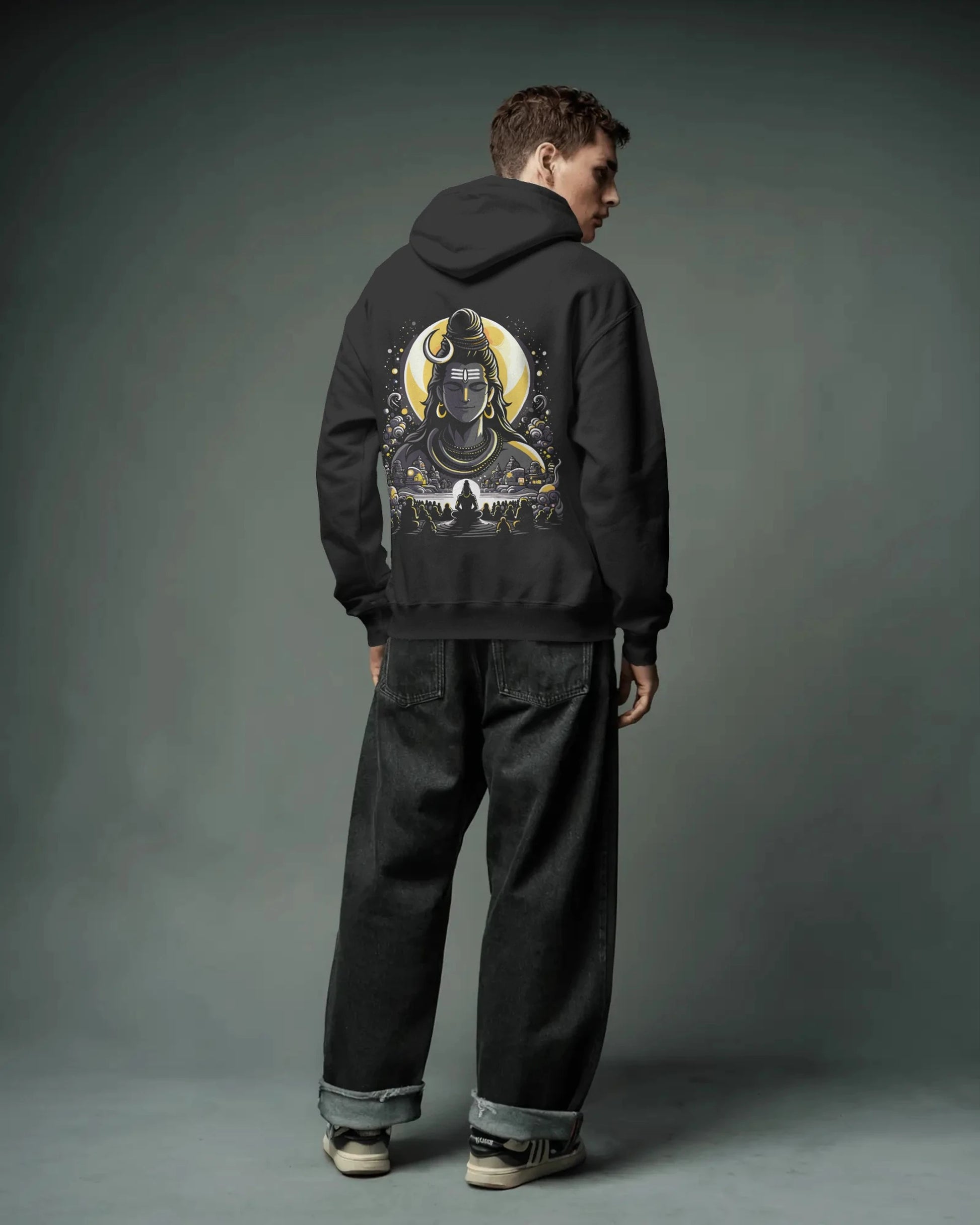 Person wearing a black pull over hoodie with a graphic design on the back against a gray background