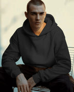 Man wearing a black pull over hoodie sitting on a bench with a blurred background
