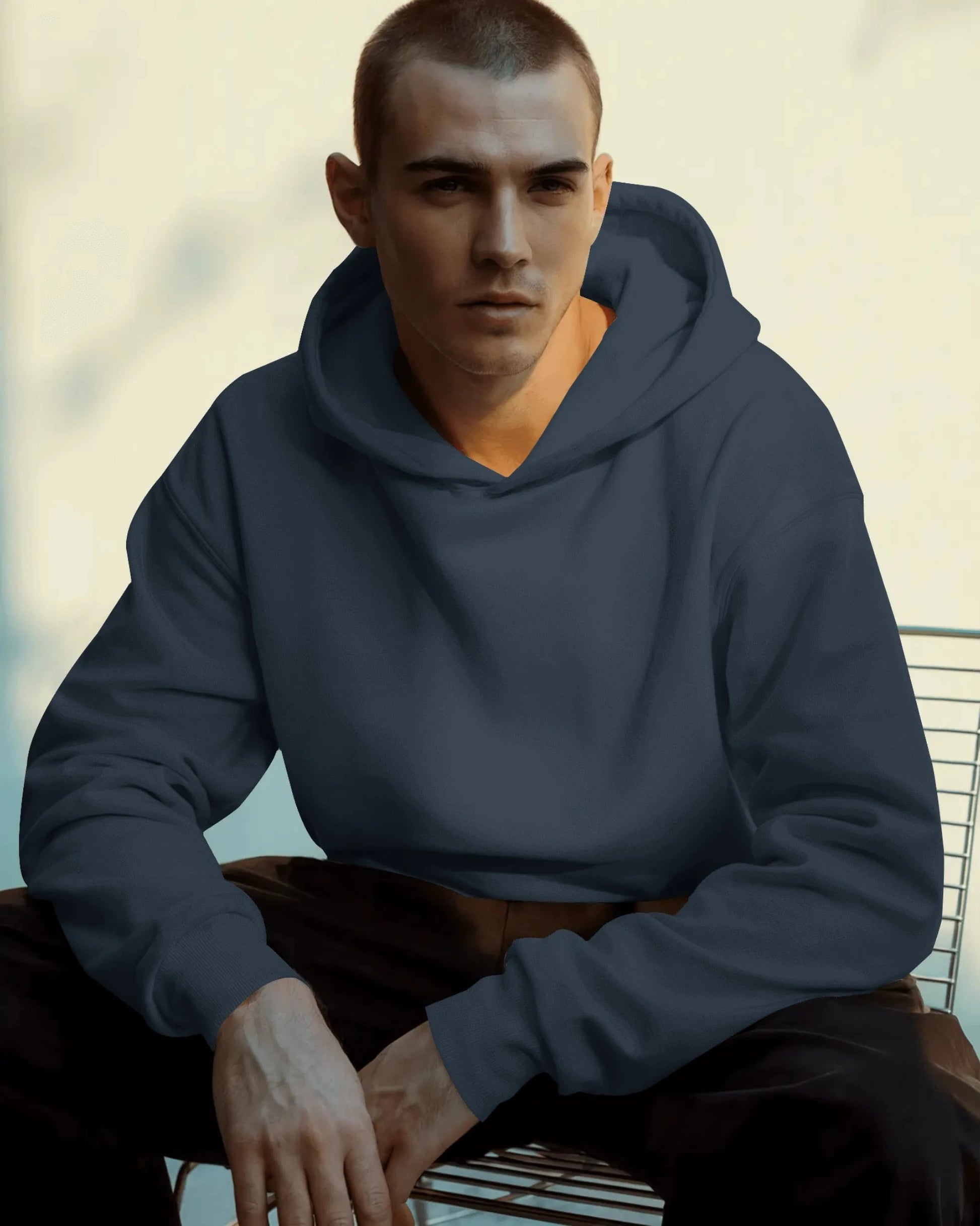Man wearing a navy blue  pull over hoodie sitting on a bench with a blurred background