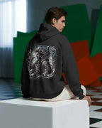 Person wearing a black Pullover hoodie with a dragon design on the back, sitting on a white cube in a modern indoor setting.