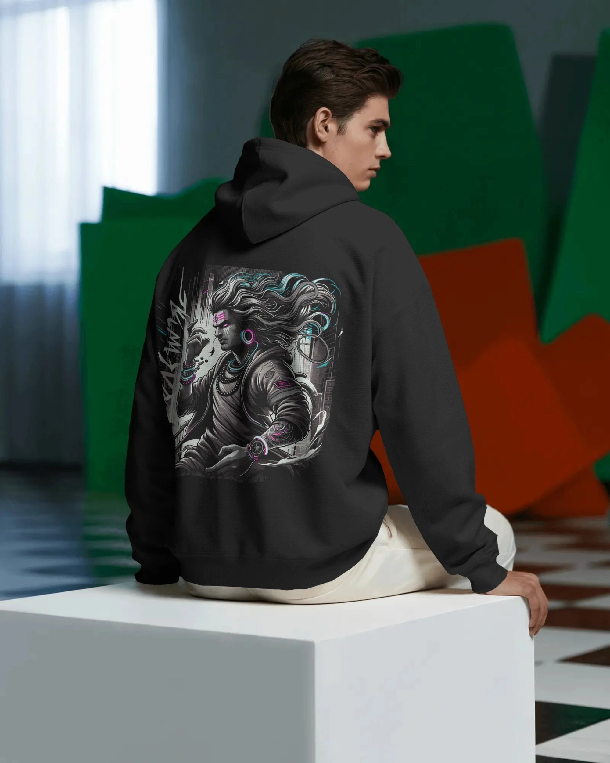 Person wearing a black Pullover hoodie with a dragon design on the back, sitting on a white cube in a modern indoor setting.